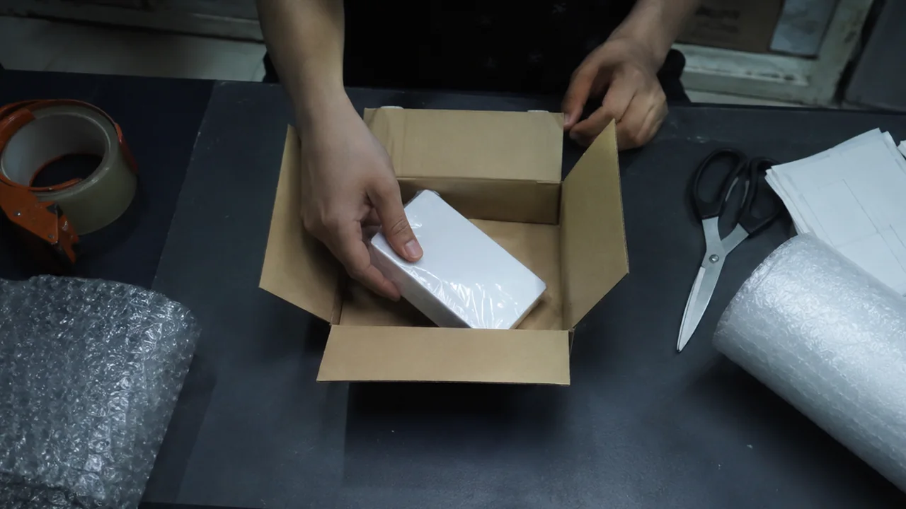 Cận cảnh bàn gói: món hàng còn nguyên seal đang được đặt vào thùng carton.